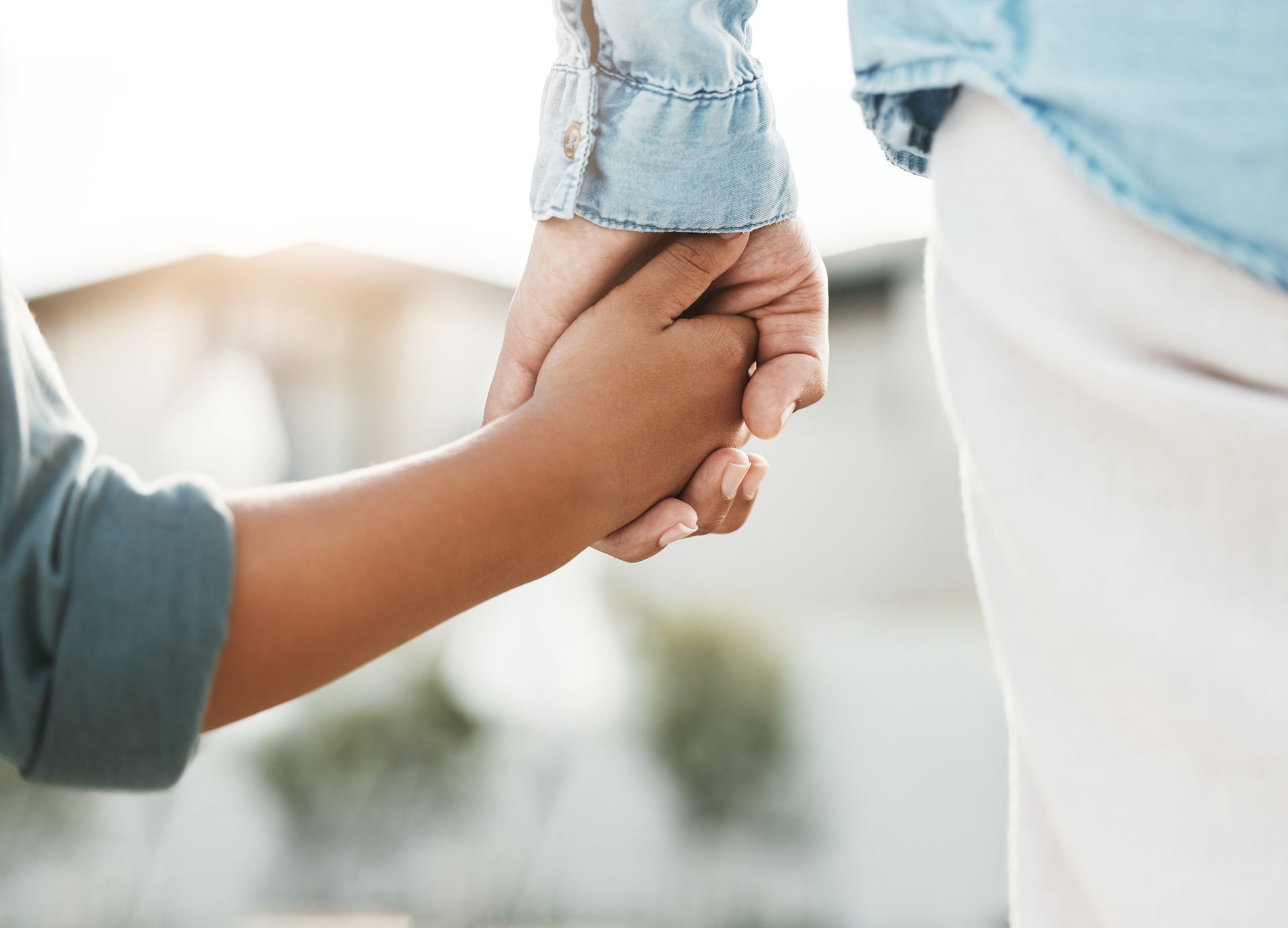 Two hands holding tightly, one small child’s hand and one adult’s hand, against a soft outdoor background Two hands holding tightly, one small child’s hand and one adult’s hand, against a soft outdoor background