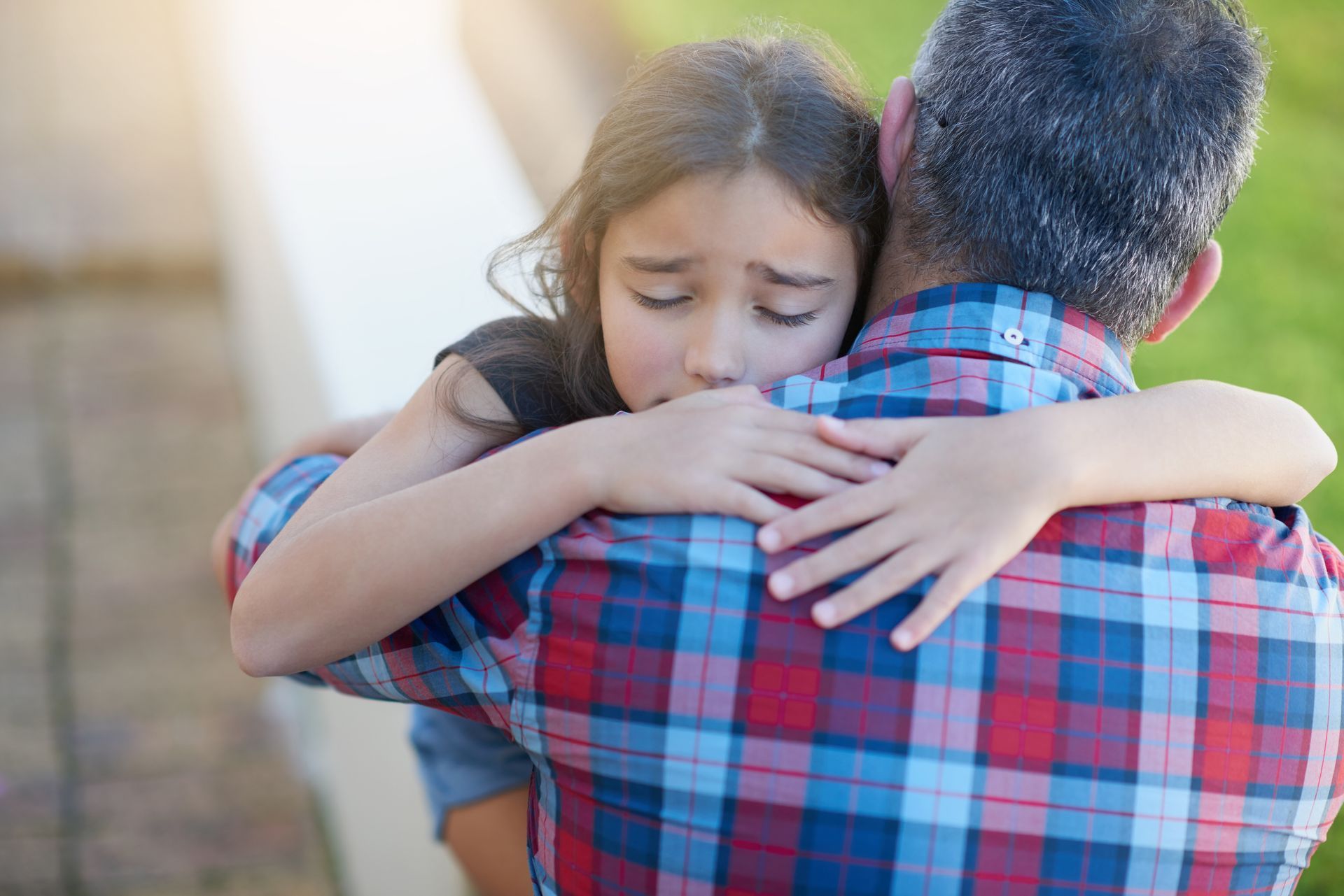 Two people hugging outdoors, one with a plaid shirt comforting the other with eyes closed Two people hugging outdoors, one with a plaid shirt comforting the other with eyes closed