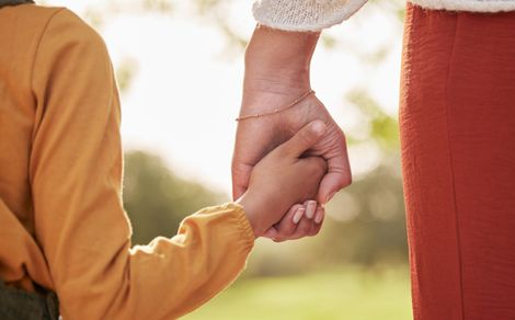 Two people holding hands outdoors, one in an orange sleeve and one in red pants. Two people holding hands outdoors, one in an orange sleeve and one in red pants.