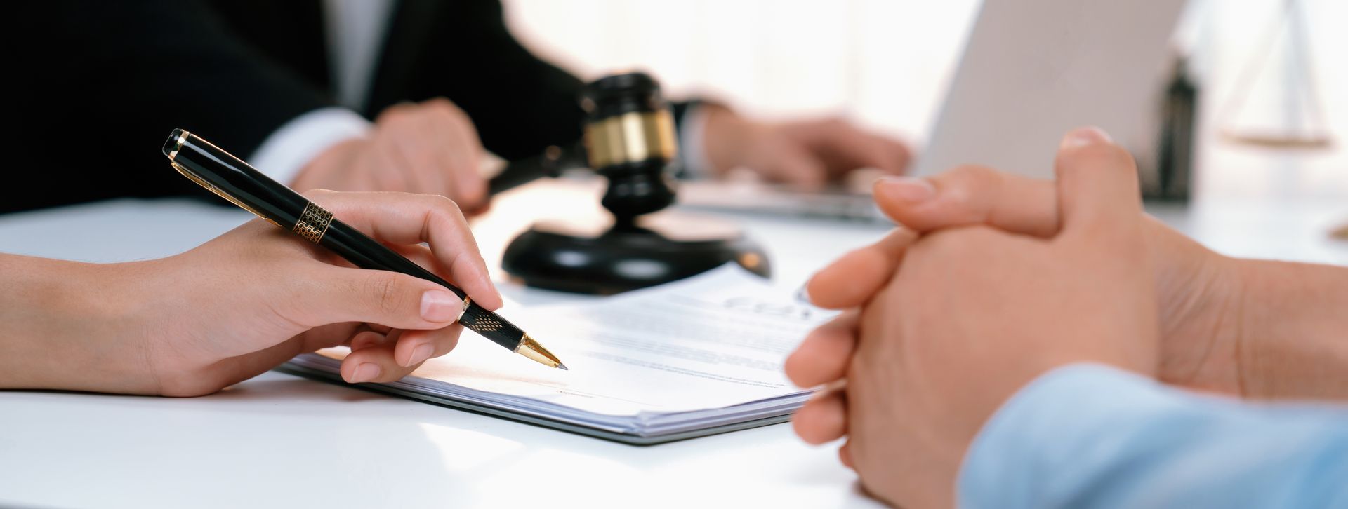 Hands reviewing documents during a meeting, with a pen, notebook, and gavel on the table. Hands reviewing documents during a meeting, with a pen, notebook, and gavel on the table.