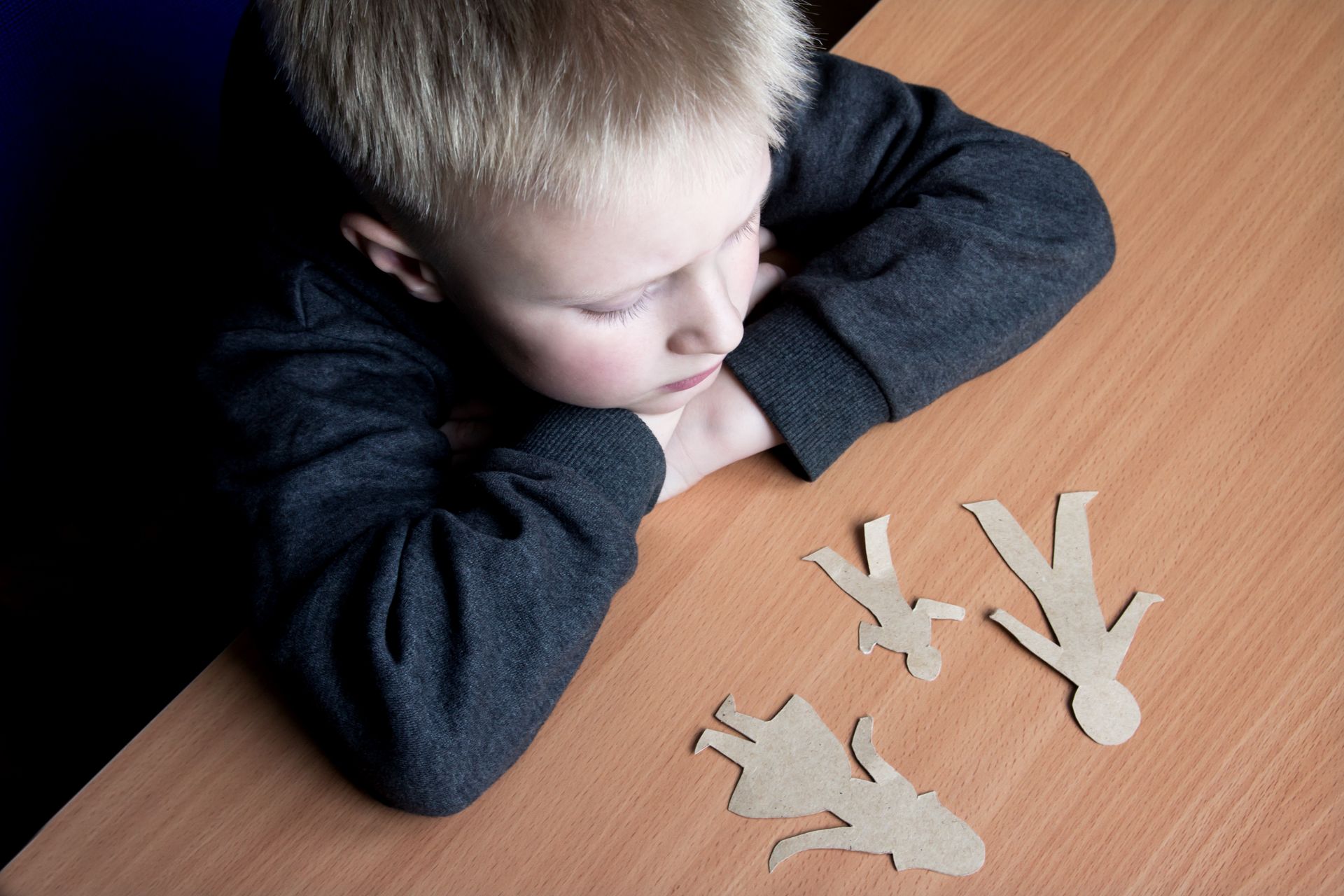 Child leaning on a table, looking at paper cutout figures on a wooden surface Child leaning on a table, looking at paper cutout figures on a wooden surface