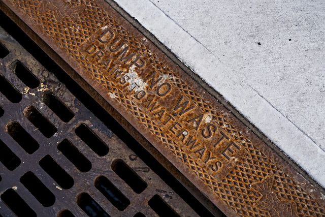 Close-up of a rusty metal storm drain cover with the words 