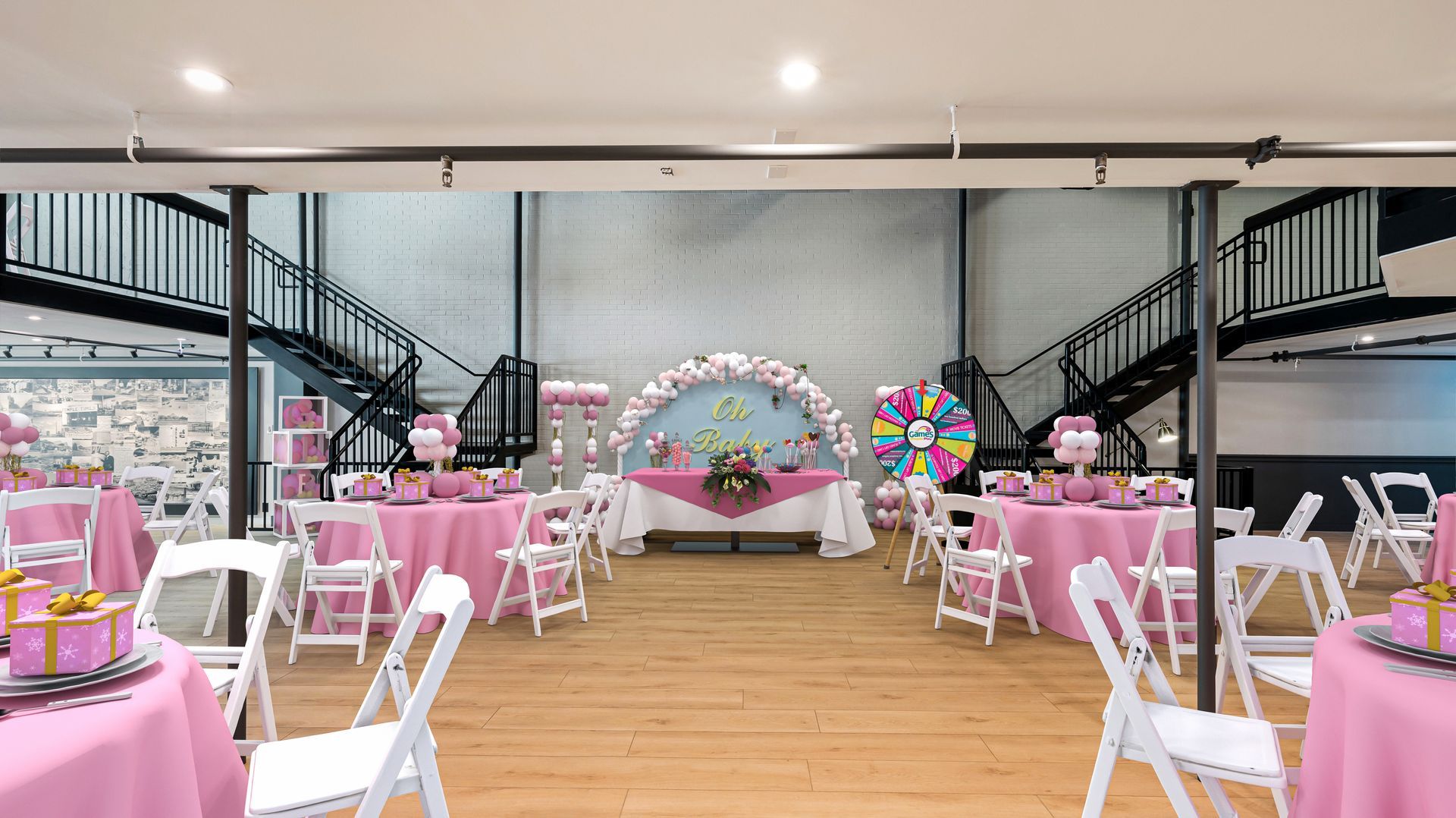 Party venue with pink table settings and balloon arch, white chairs, wooden floor, brick and metal staircase.