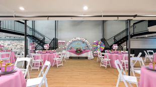 Pink-themed party in a venue with exposed brick, decorated tables, balloon arch, stairs on both sides.
