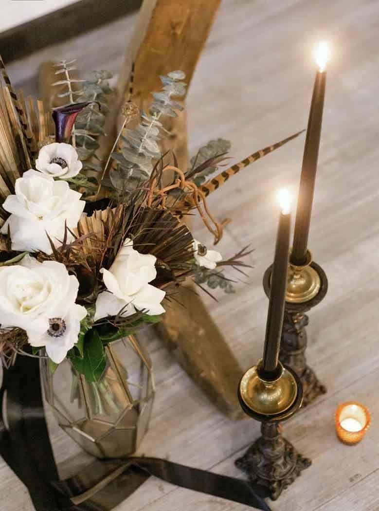 Floral arrangement with white flowers, feathers, and candles in holders, on a wood surface.