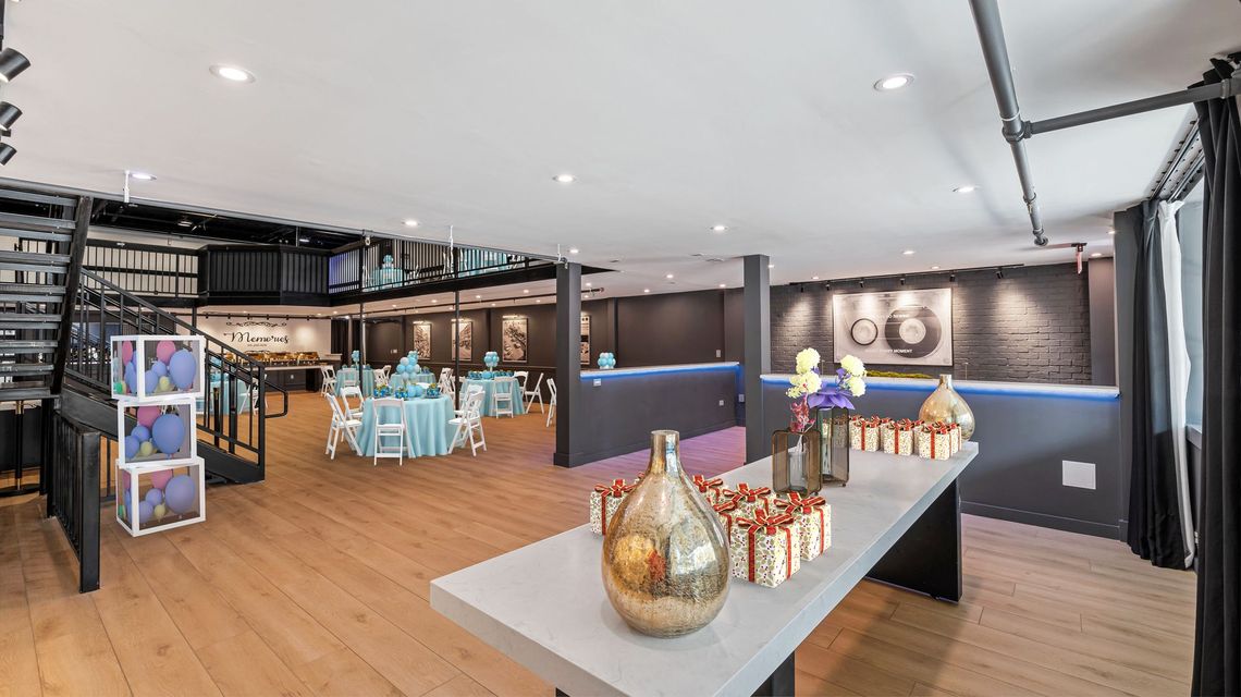 Reception hall with tables, decorations, and a buffet. Hardwood floors and dark walls with modern decor.