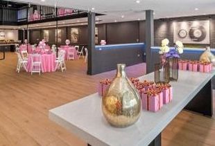 Event space with pink tables, decor, and a buffet table. A large golden vase is in the foreground.