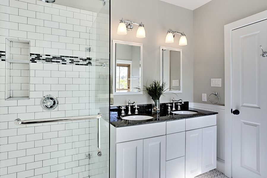 Bathroom remodel with glass shower, white tile, black countertop, and double vanity lights