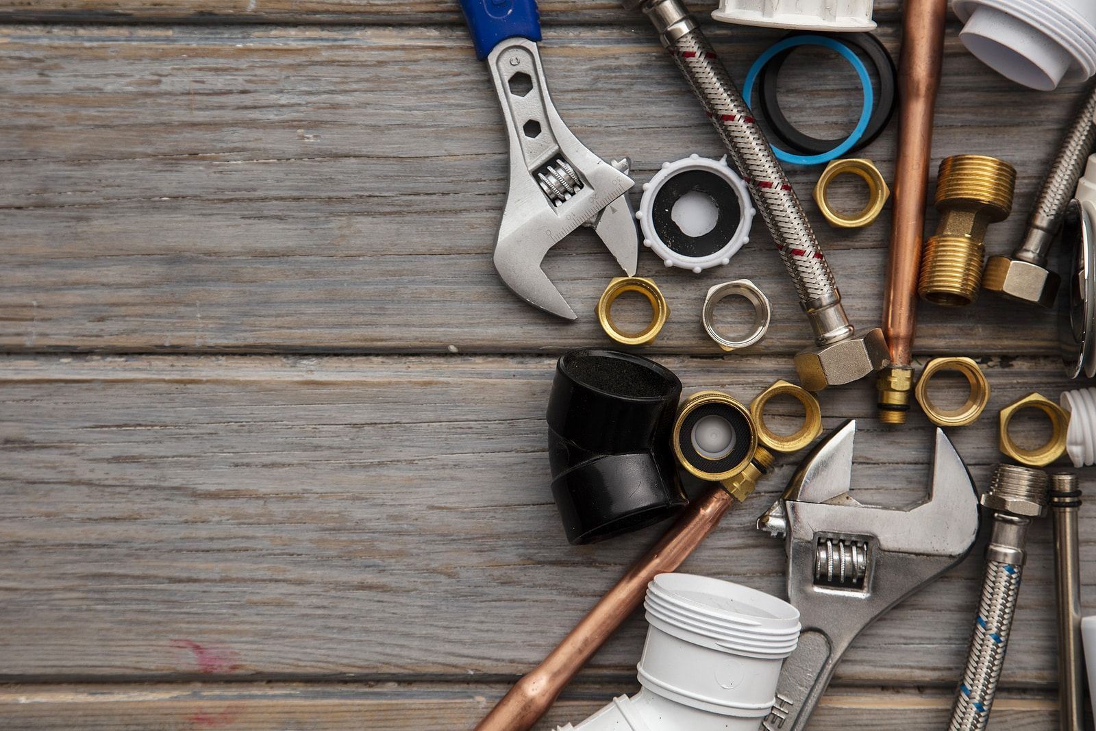 Assorted plumbing tools and fittings on weathered wood, including wrenches, pipes, and tape measure