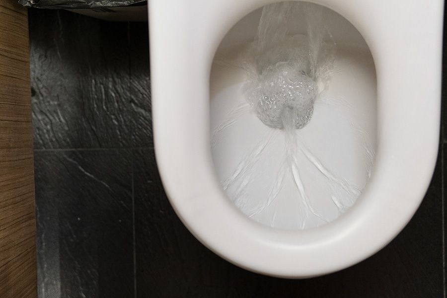White toilet bowl with water on a dark floor, viewed from above