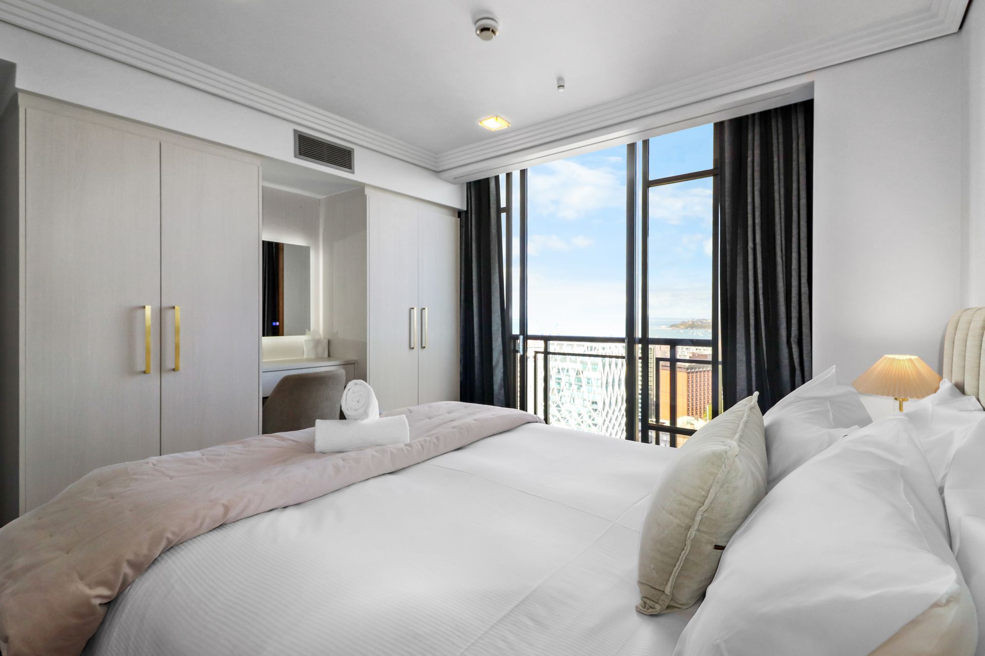 Bedroom with a large bed, closet, dressing table, and a balcony with a city view.