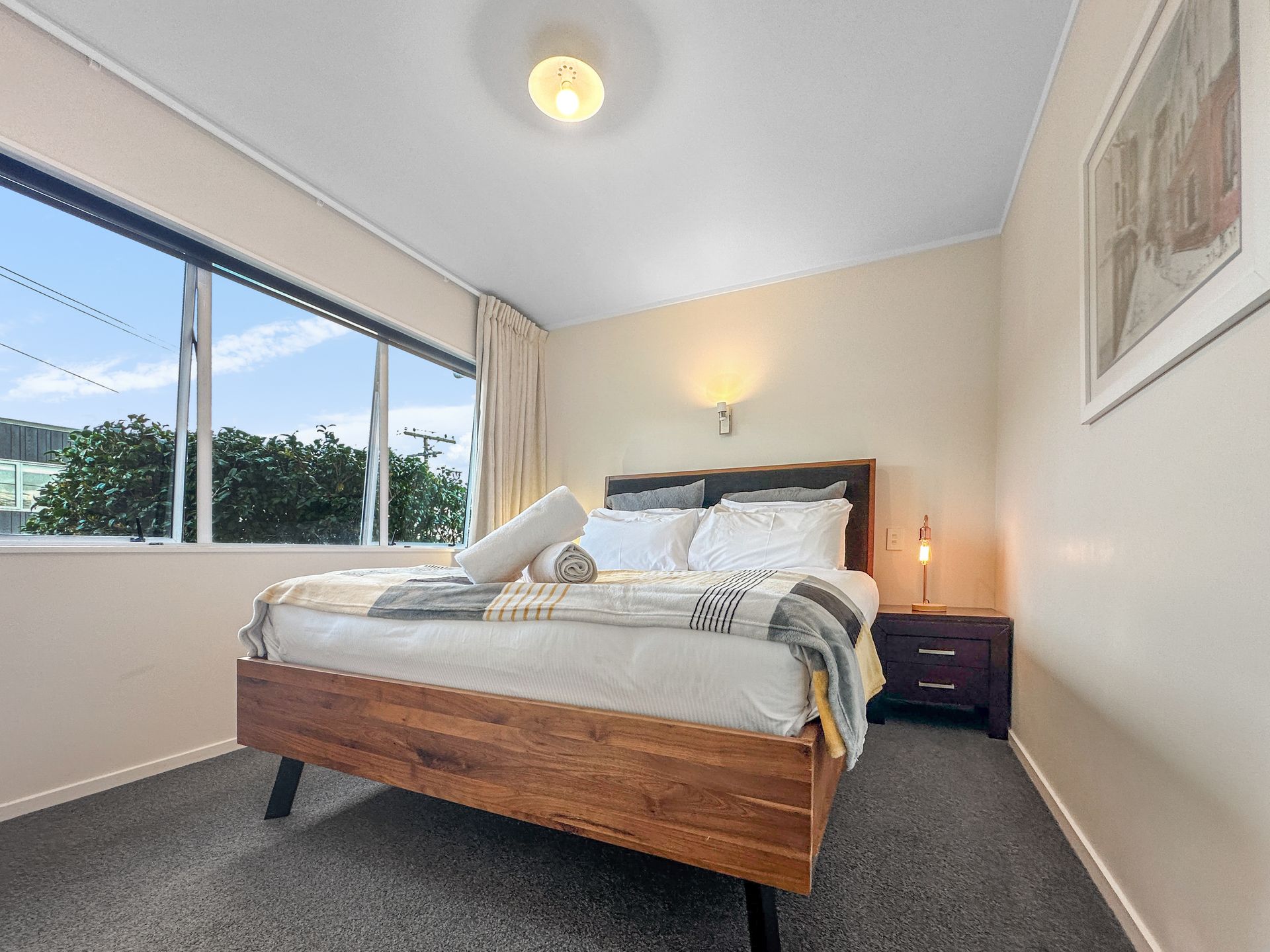 Bedroom with a wooden bed frame, window, and neutral-toned walls.