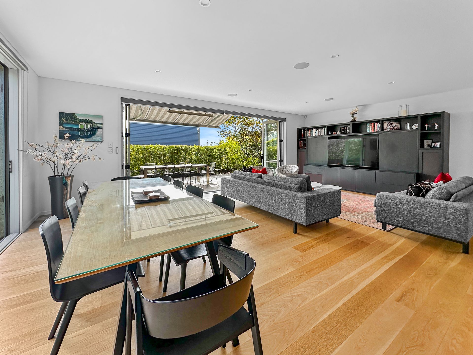 Open-plan living space with dining table, grey sofas, entertainment unit, and outdoor access.