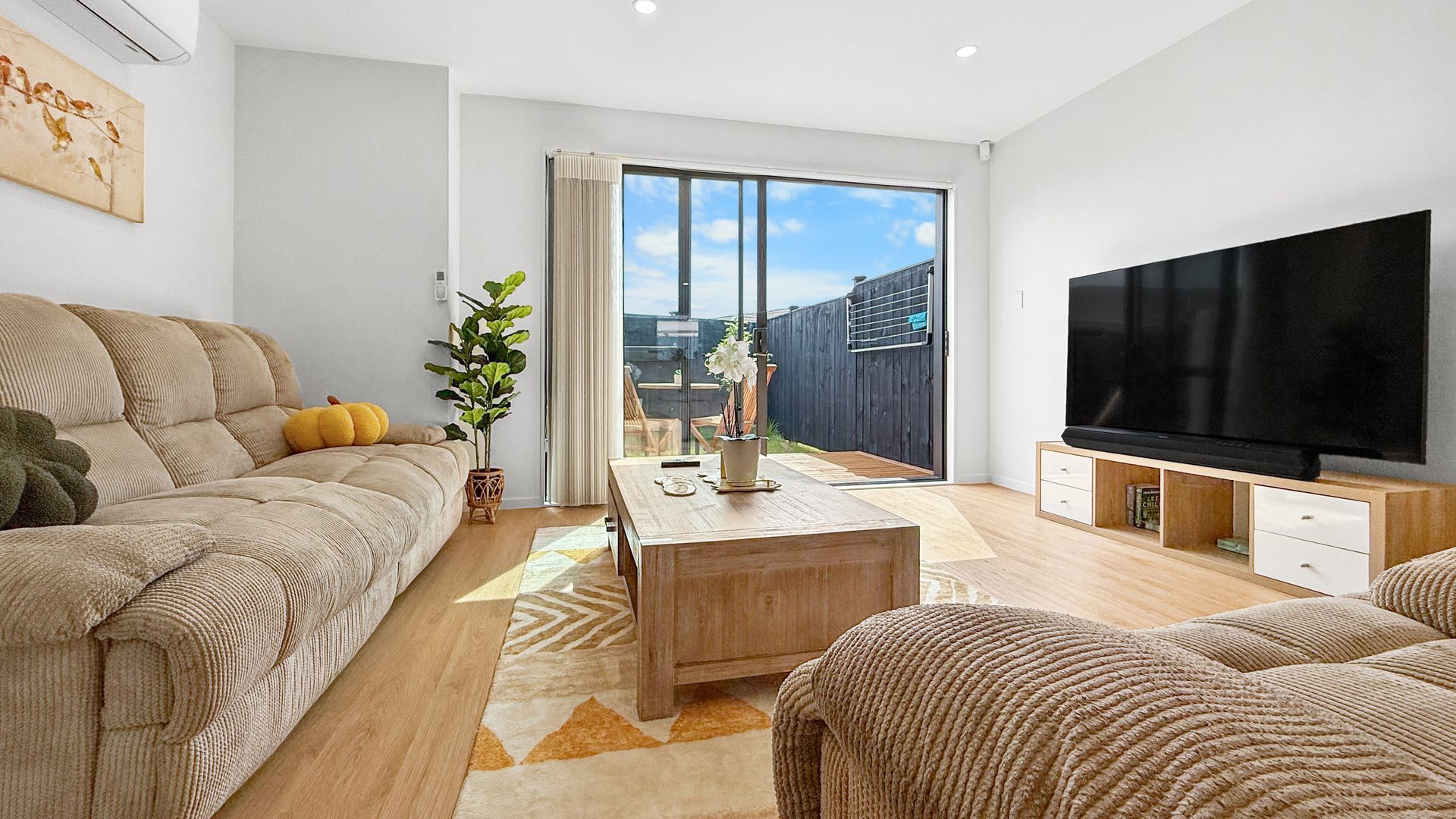 Cozy living room with corduroy sofa, TV, and sliding door to small yard. Wooden furniture and warm tones.