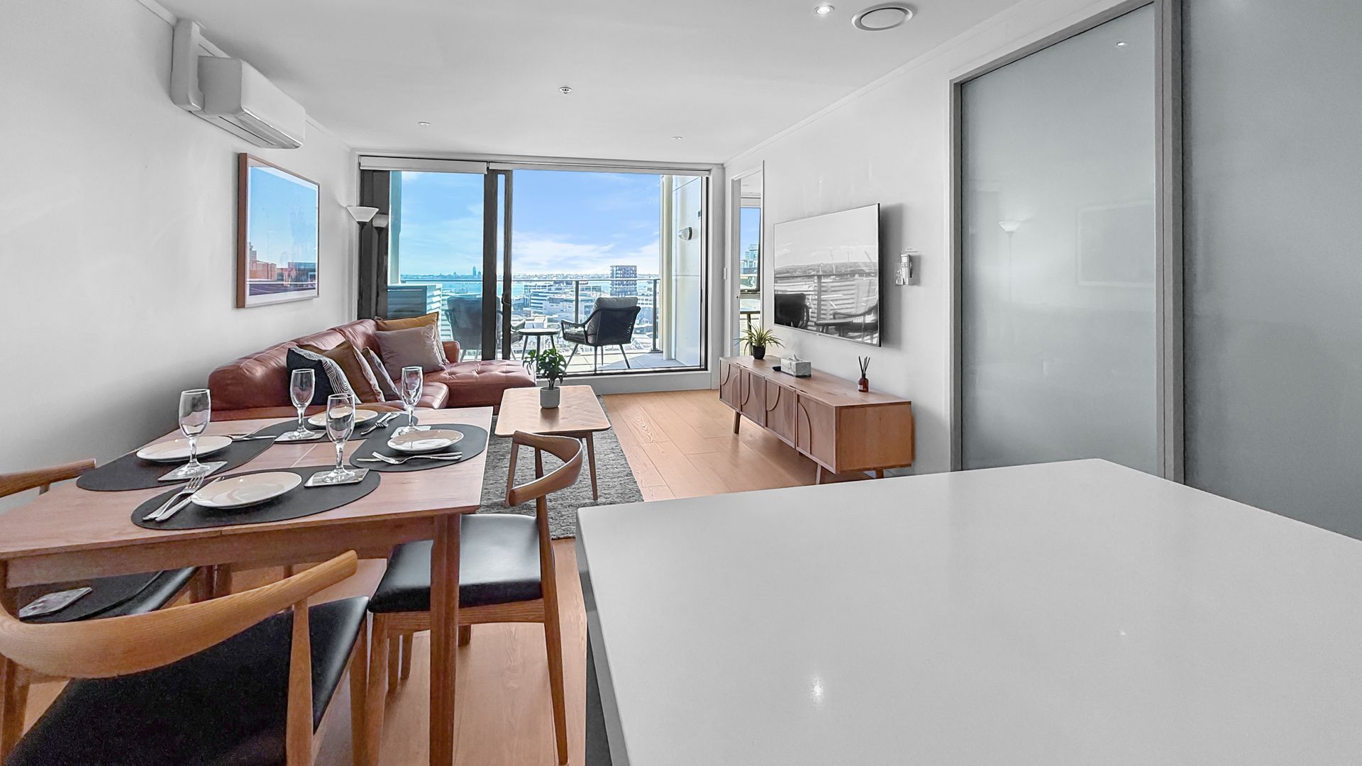 Modern apartment living room with dining table, sofa, balcony and city view.