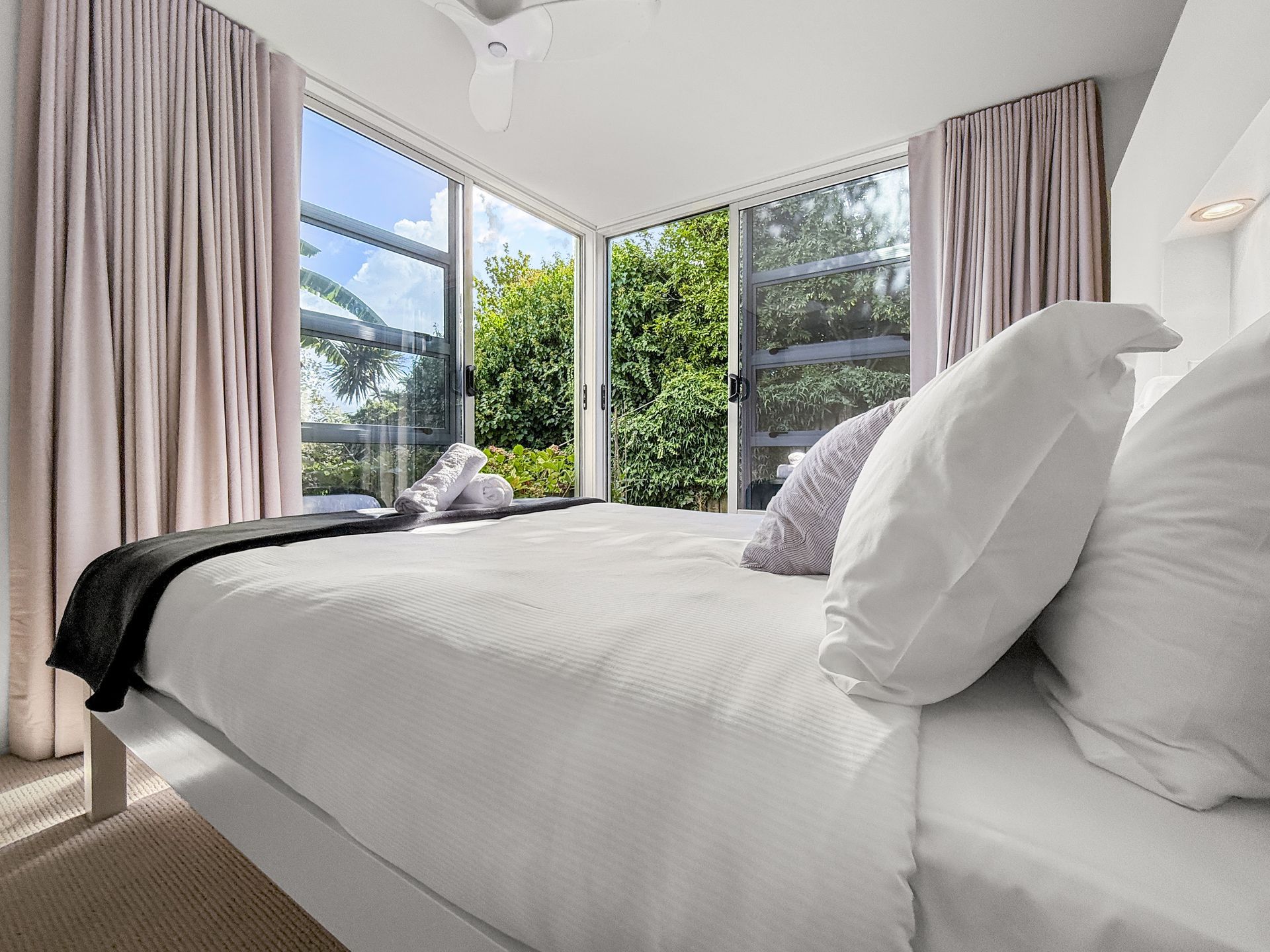 Bedroom with white bed, sheer curtains, and sliding glass door to a green outdoor view.