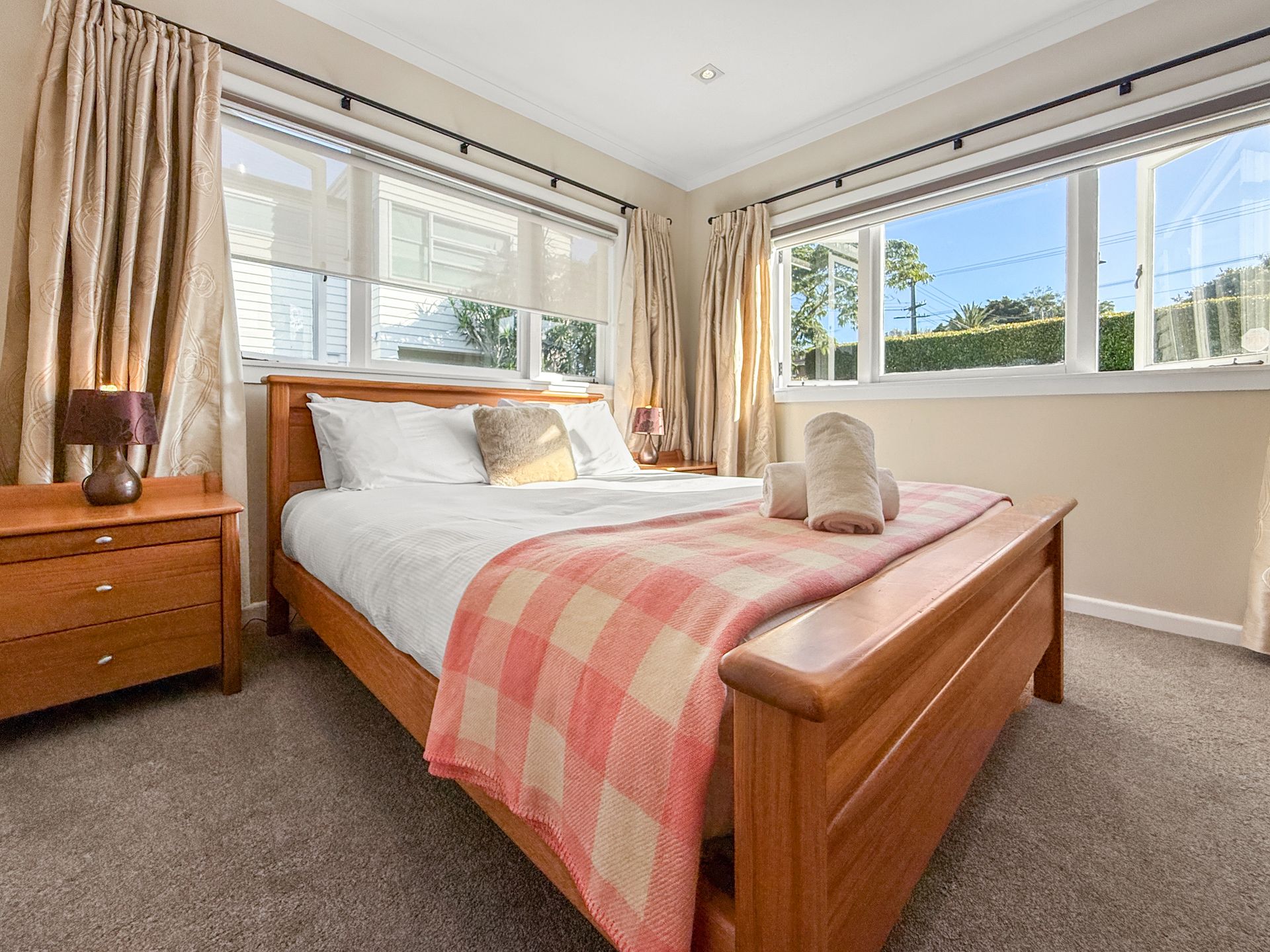 Bedroom with a wooden bed, nightstand, and windows with tan curtains; light brown carpet.