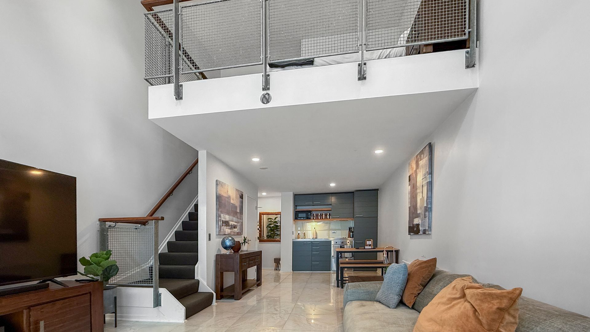 Modern living room with a mezzanine level and dark staircase.