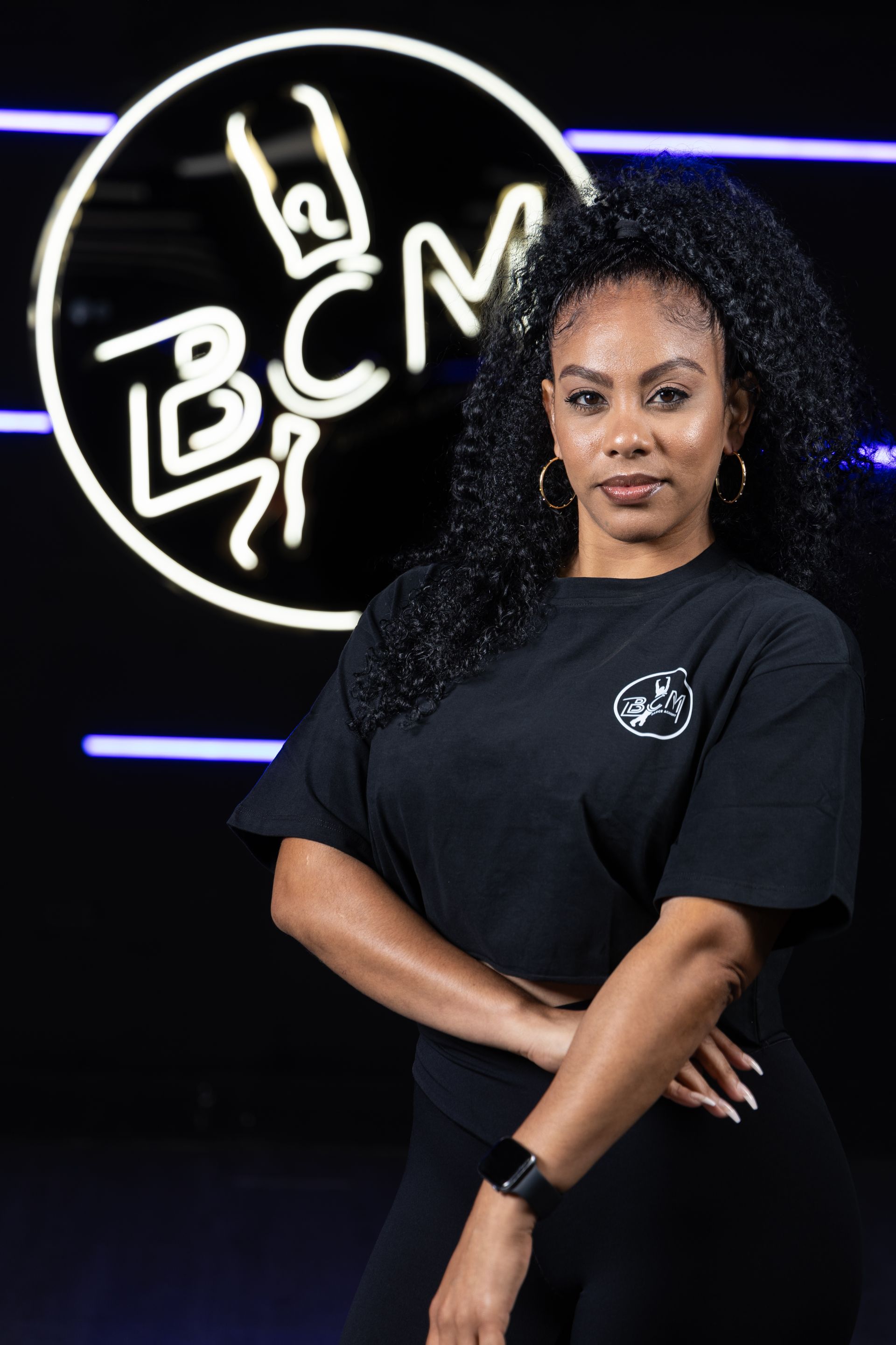 A woman in a black shirt is standing in front of a neon sign.