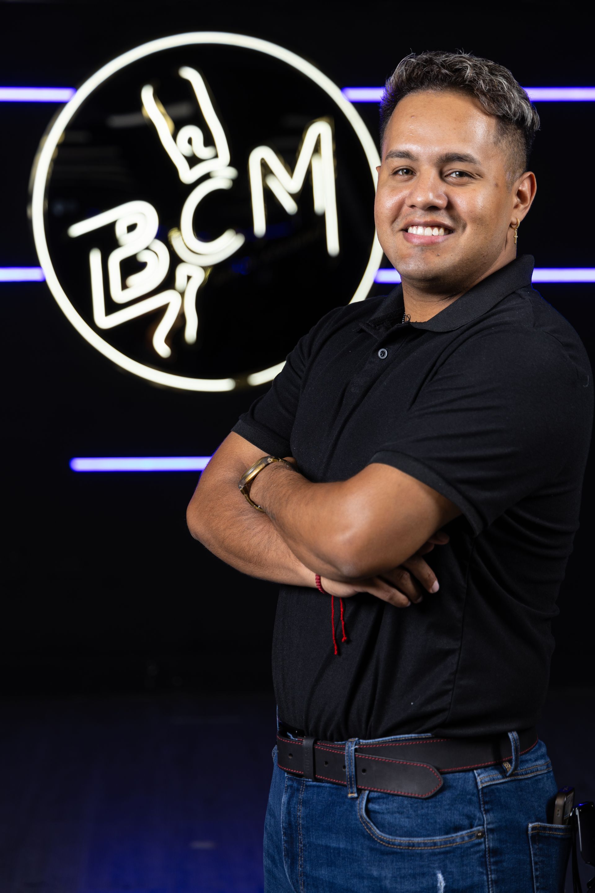 A man is standing with his arms crossed in front of a bcm logo.