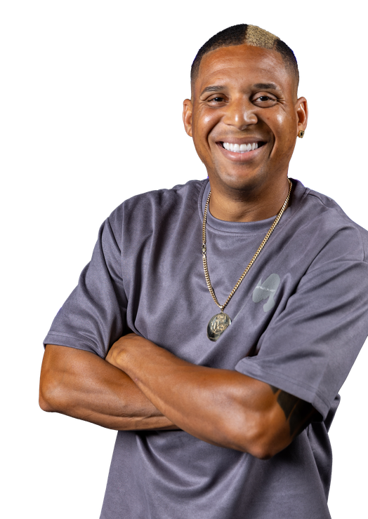 A man wearing a gray shirt and a gold necklace is smiling with his arms crossed.