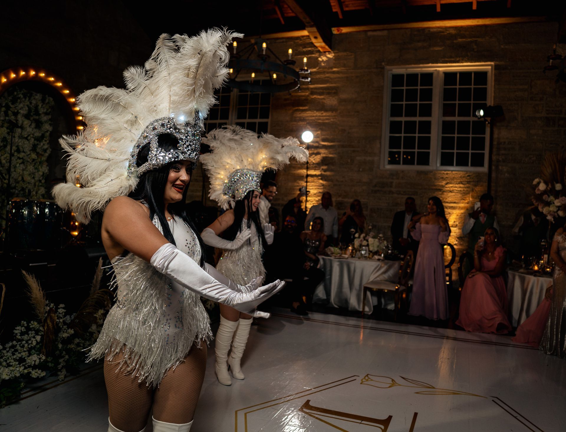 A group of women in feathered costumes are dancing on a dance floor at a wedding reception.