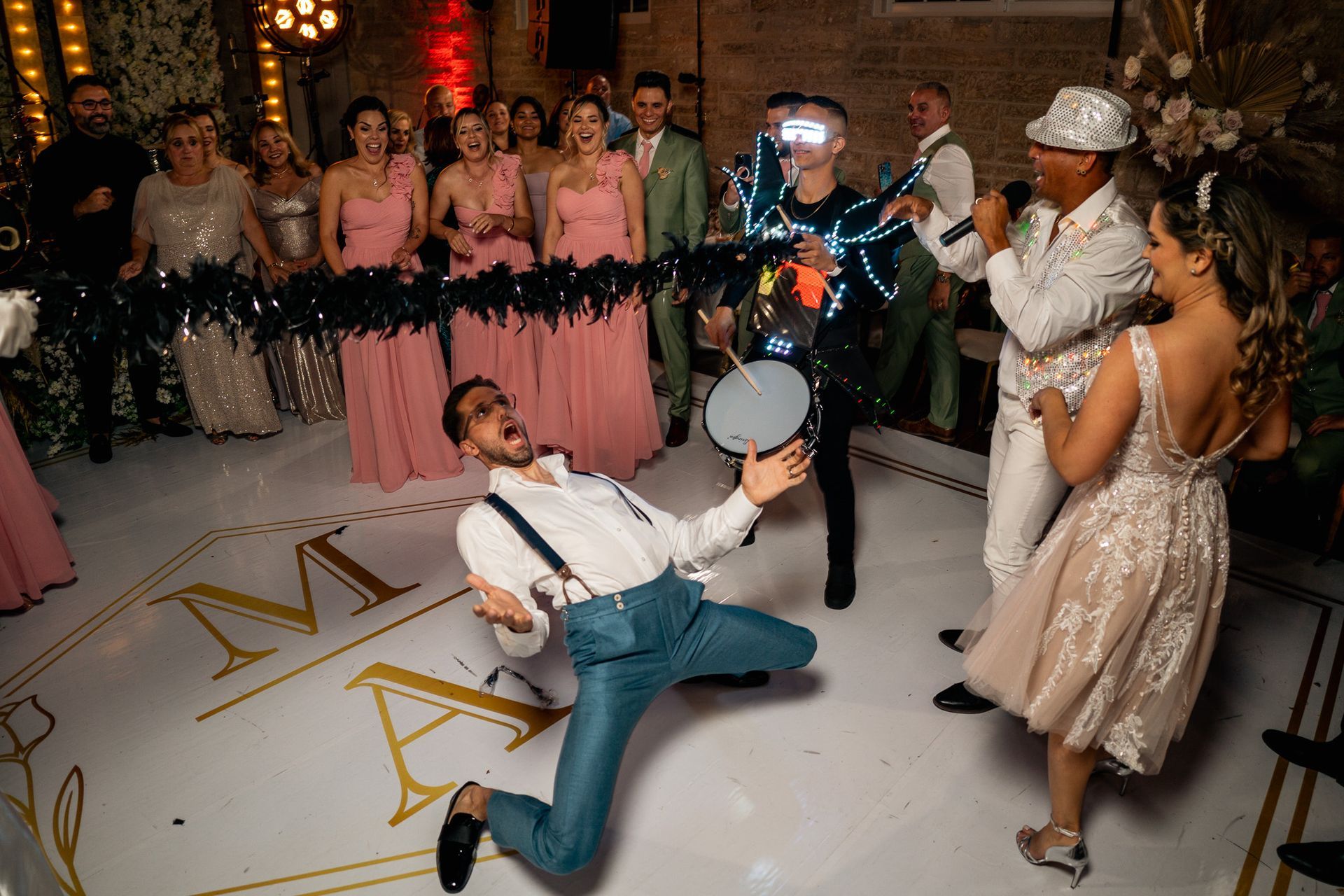 A man is kneeling on the floor playing a drum at a wedding reception.