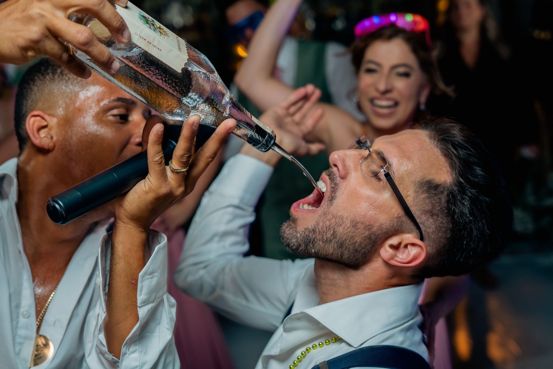 A man is drinking from a bottle at a party.