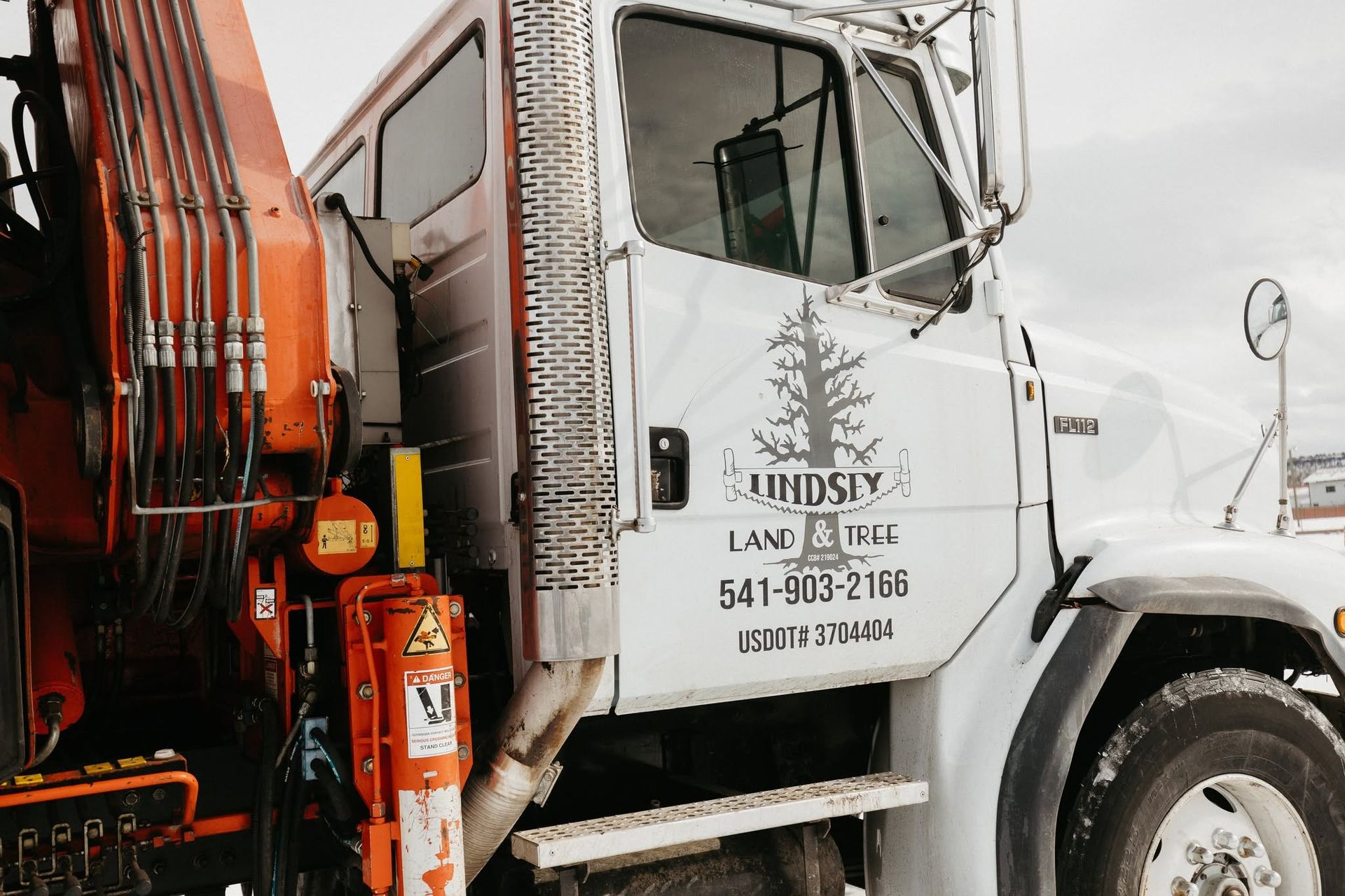 White dump truck cab with company logo and phone number, parked beside an orange excavator in snowy conditions