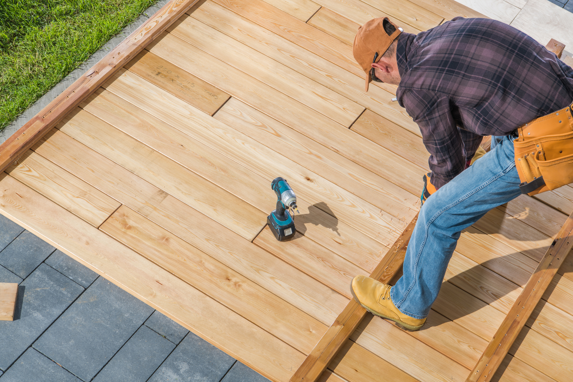 Worker installing wooden deck boards with a power drill outdoors.