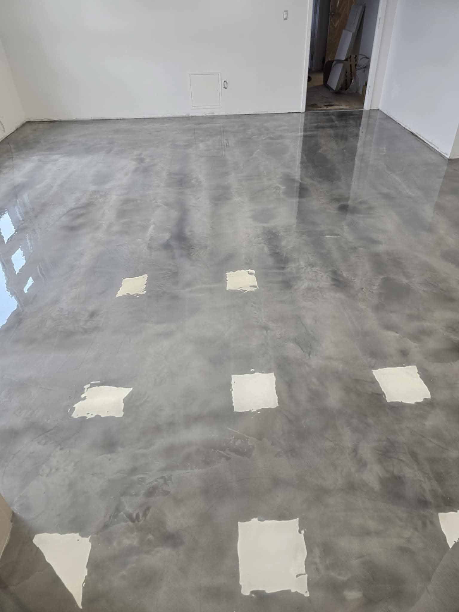 Une pièce au sol en époxy gris métallisé poli qui reflète la lumière. Des carrés blancs sont disséminés sur le sol.