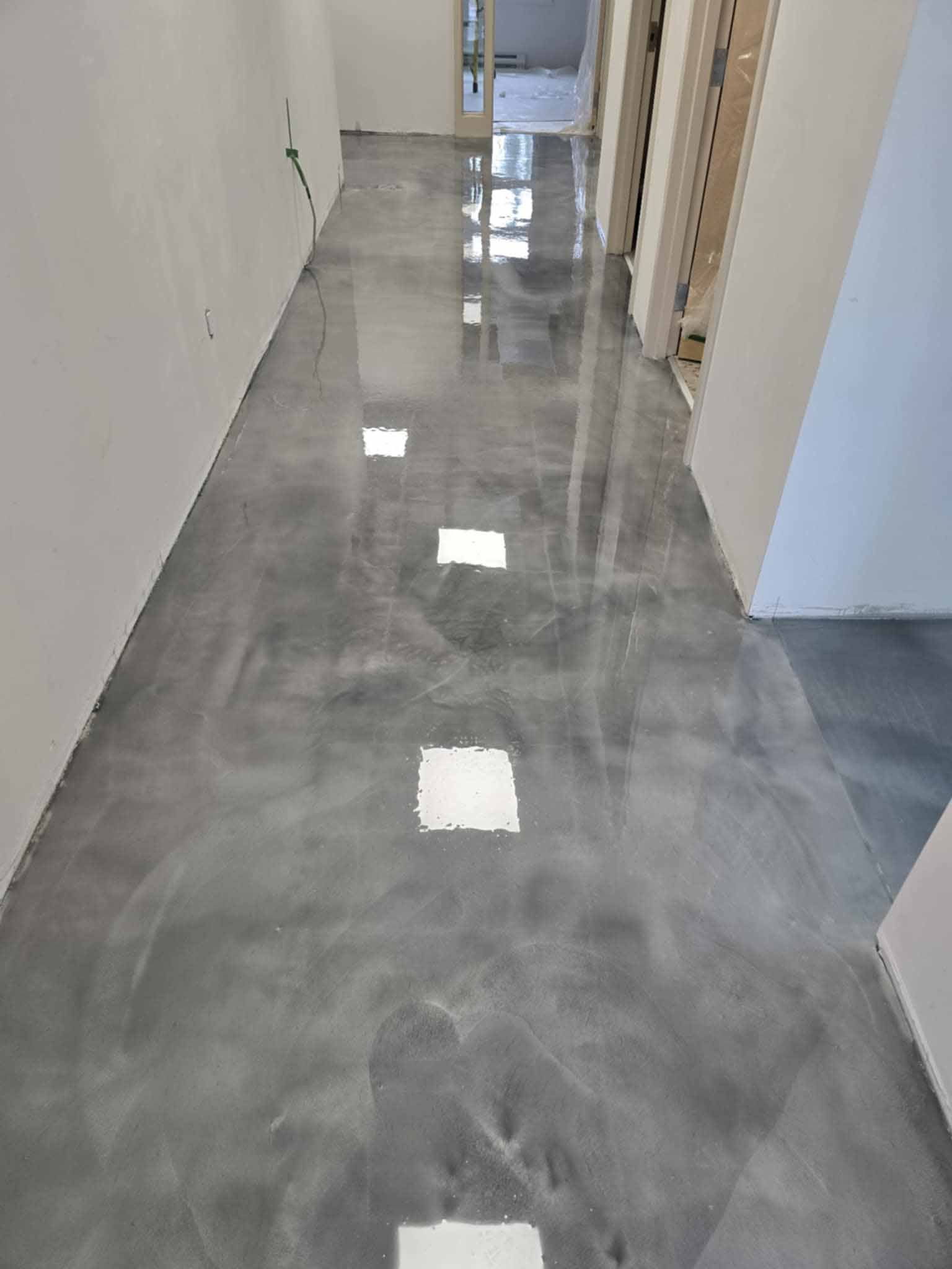 Sol en époxy gris dans un couloir aux murs et portes blancs, reflétant la lumière ambiante.