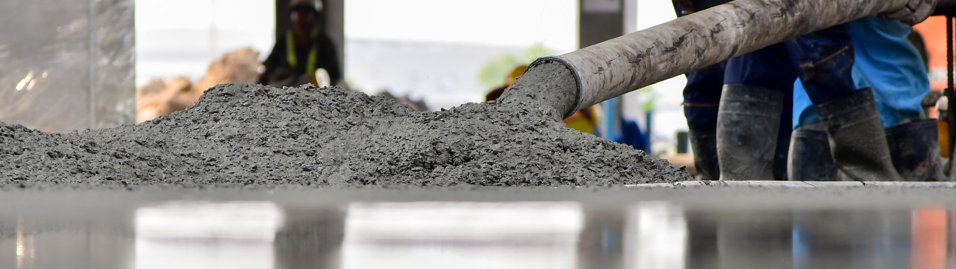 Du béton est déversé à l'aide d'un tuyau sur une surface réfléchissante ; des ouvriers du bâtiment sont visibles en arrière-plan.