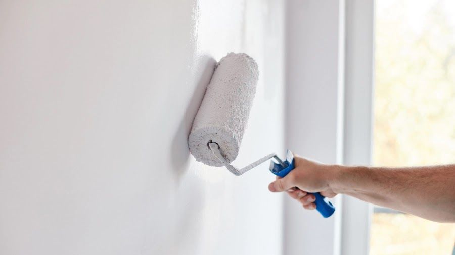 A person is painting a wall with a paint roller.