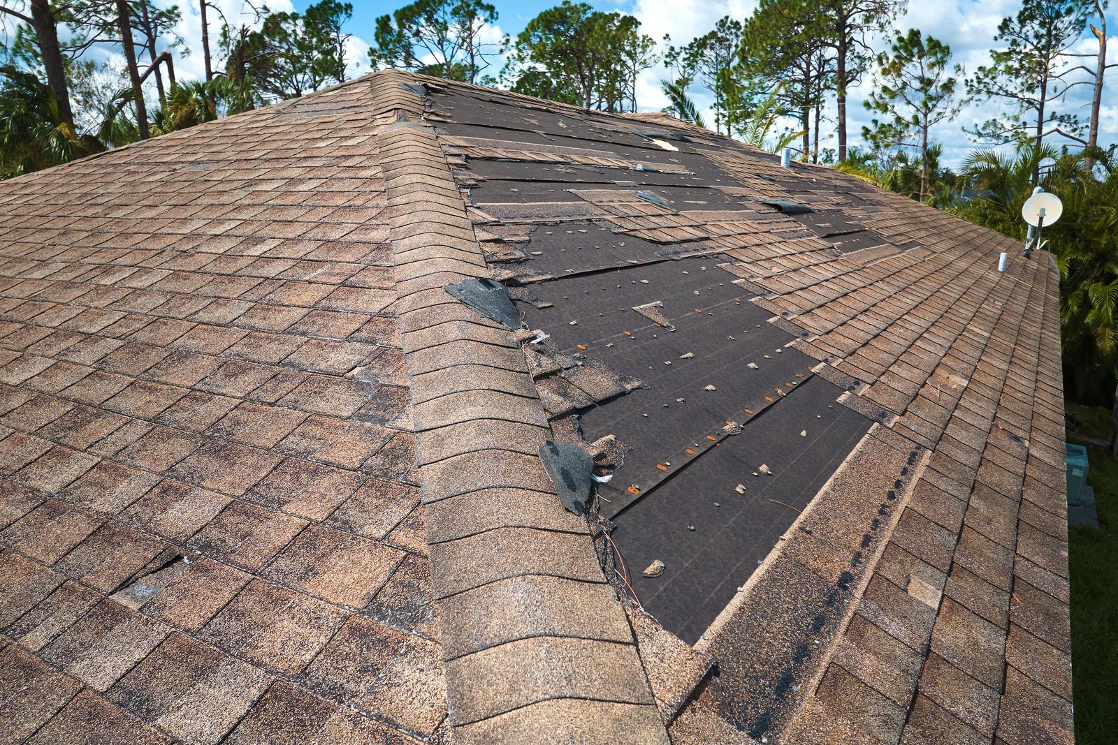A roof with shingles missing and a satellite dish on top of it.