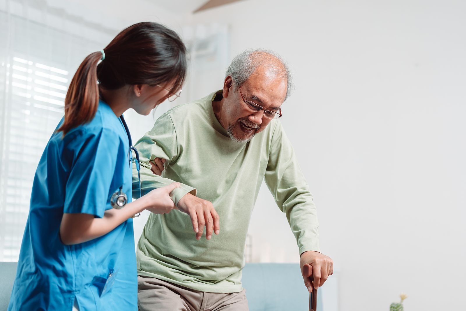 A nurse is helping an elderly man walk with a cane.
