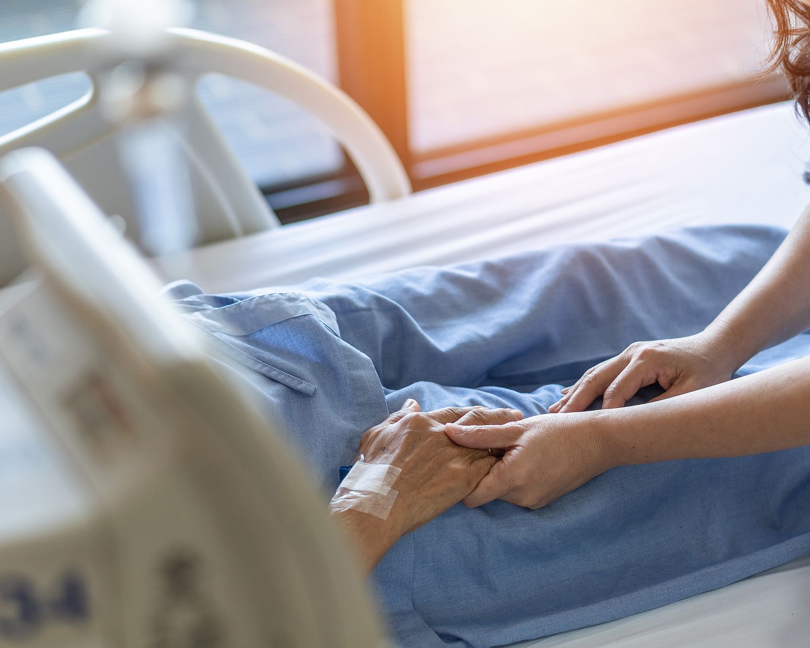 A woman is holding the hand of a patient in a hospital bed.