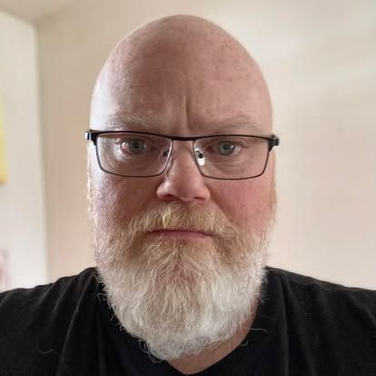 A bald man with a beard and glasses is wearing a black shirt.