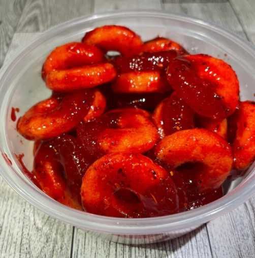 Sliced strawberries in syrup in a clear plastic container on a gray table