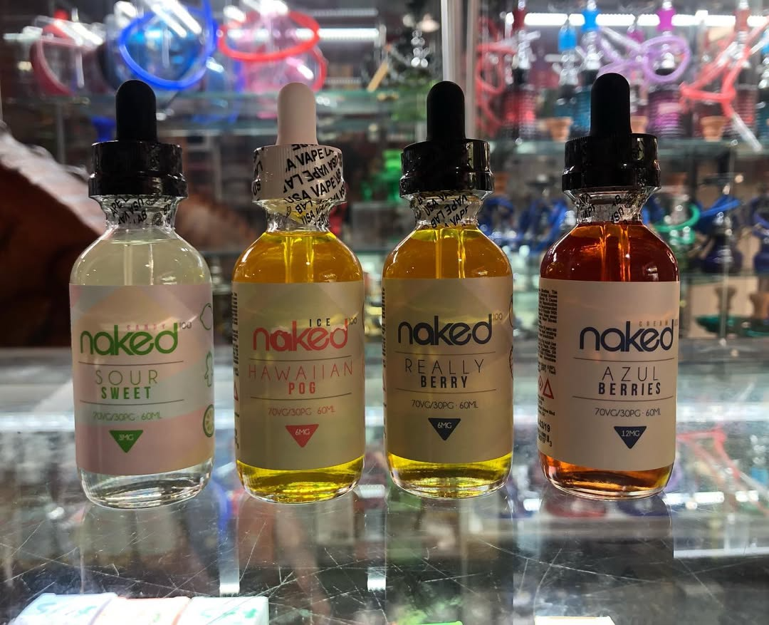 Four Naked vape juice bottles in green, yellow, and amber on a reflective shelf.
