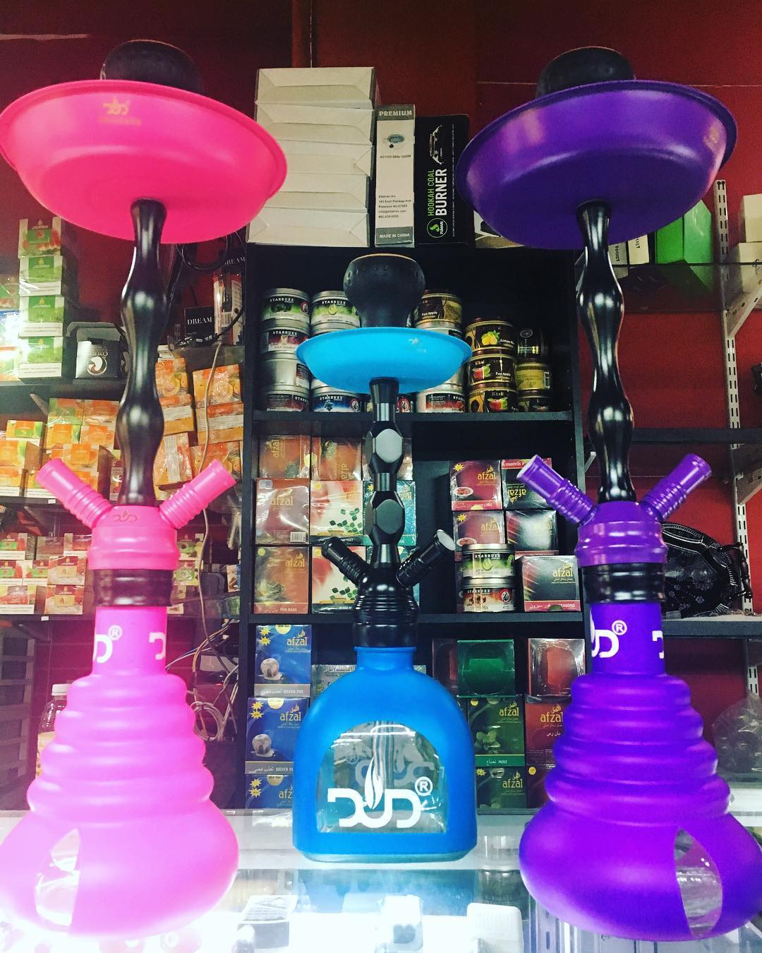 Three colorful hookah pipes—pink, blue, and purple—displayed on shelves in a shop.