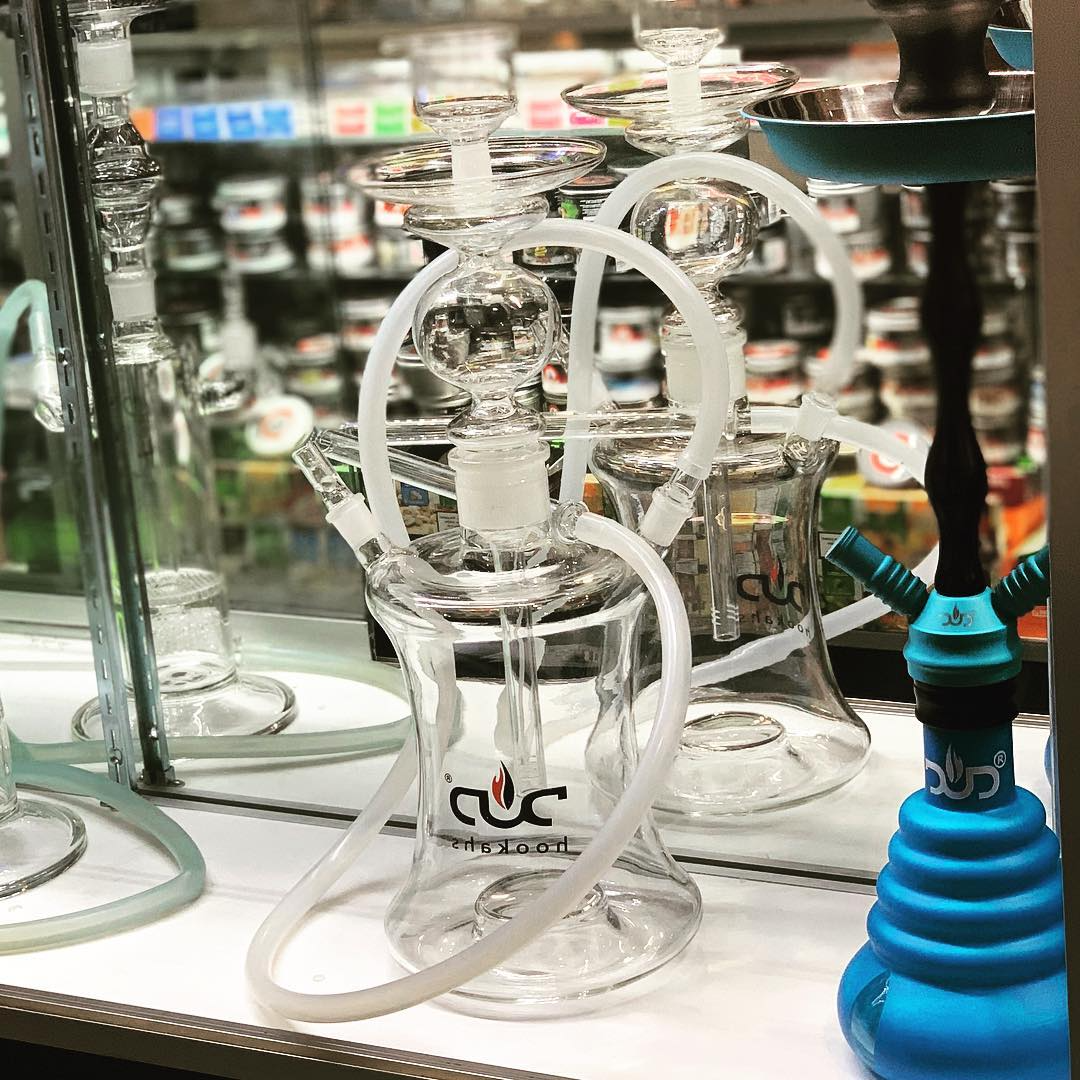 Glass hookah with white hoses on a table in a shop, with blue and black parts in the foreground.