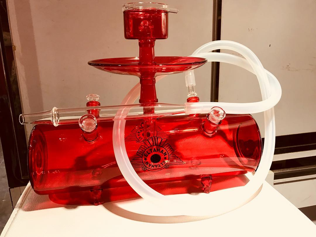 Red translucent plastic toy with white tubing on a tabletop, shaped like a small fountain or castle.