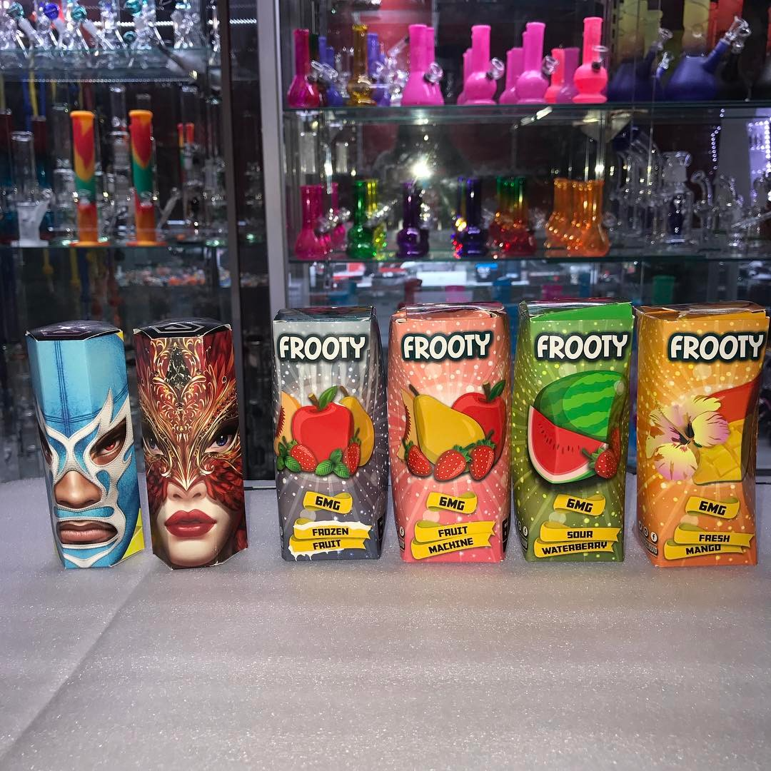Colorful glass bong display with lucha mask decor and four fruity vape boxes on a shelf