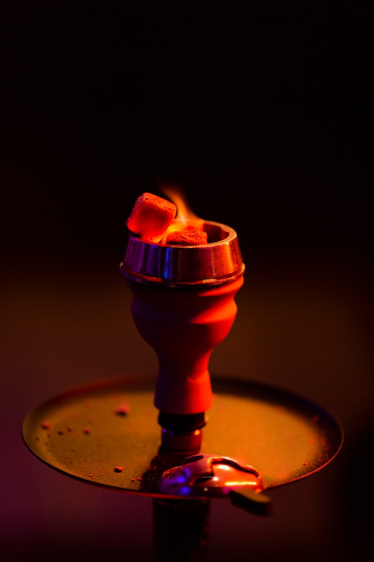 Lit hookah bowl glowing red on a tray in dim, warm light