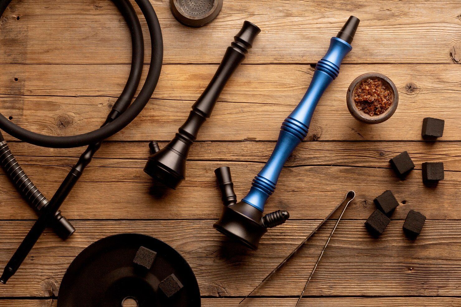 Hookah parts on a wooden table, including blue and black stems, hose, charcoal, and tobacco bowl.