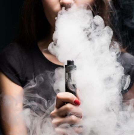 Person holding a vape device with thick white vapor billowing around their face and hand