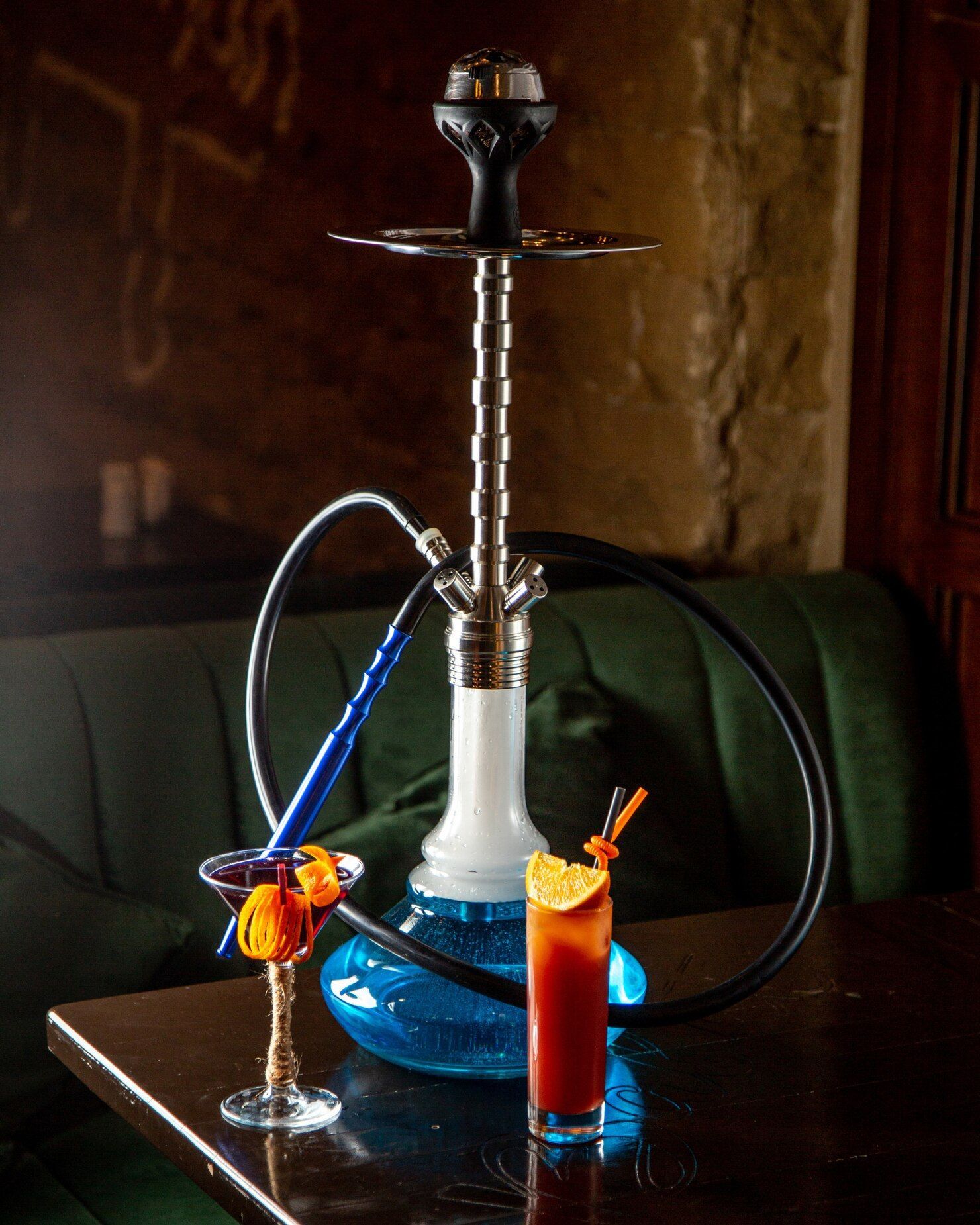 Blue hookah with two colorful drinks on a table in a dimly lit room