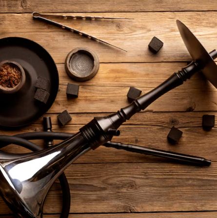 Wooden hookah setup with black hose and charcoal pieces on a rustic wooden table.