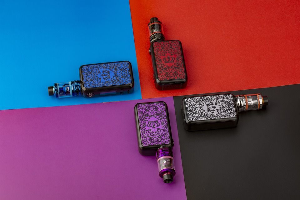 Four colorful vape devices arranged on blue, red, purple, and black backgrounds.